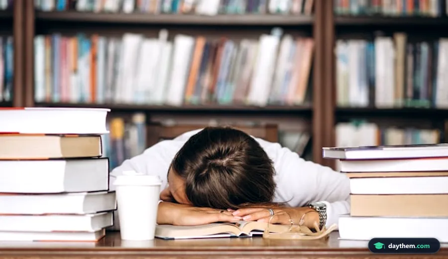 Học sinh gục đầu mệt mỏi trên bàn học với chồng sách vở lớn