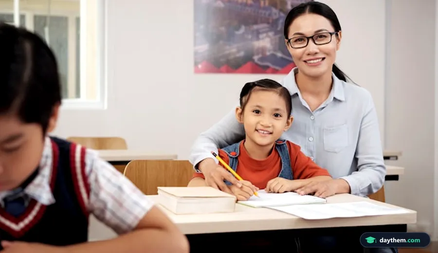 Gia sư đang cúi người hướng dẫn bài học cho học sinh tại bàn làm việc