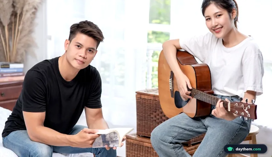 Nữ sinh viên chơi đàn guitar cùng bạn nam cầm sách hát trong buổi sinh hoạt câu lạc bộ nghệ thuật và âm nhạc tại trường đại học